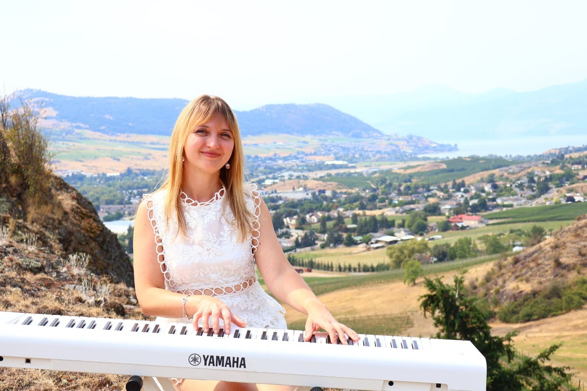 Iryna Viriasova in a white dress at a keyboard overlooking Vernon, British Columbia.
